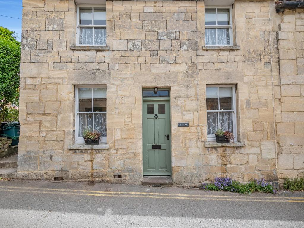 a stone building with a green door and two windows at Wayside in Painswick