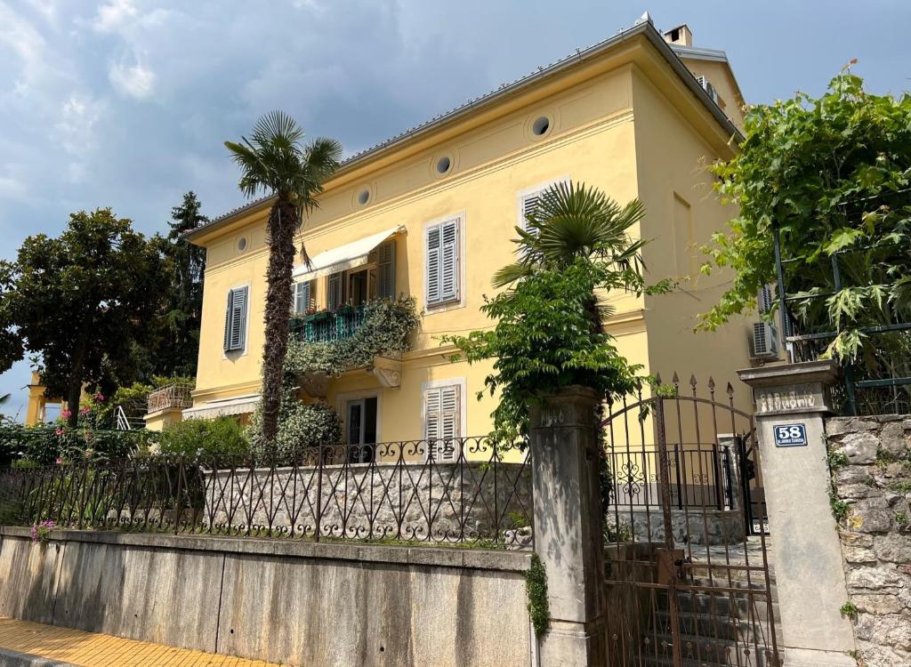 une maison jaune avec une clôture et un palmier dans l'établissement Apartments by the sea Opatija - Volosko, Opatija - 7846, à Volosko