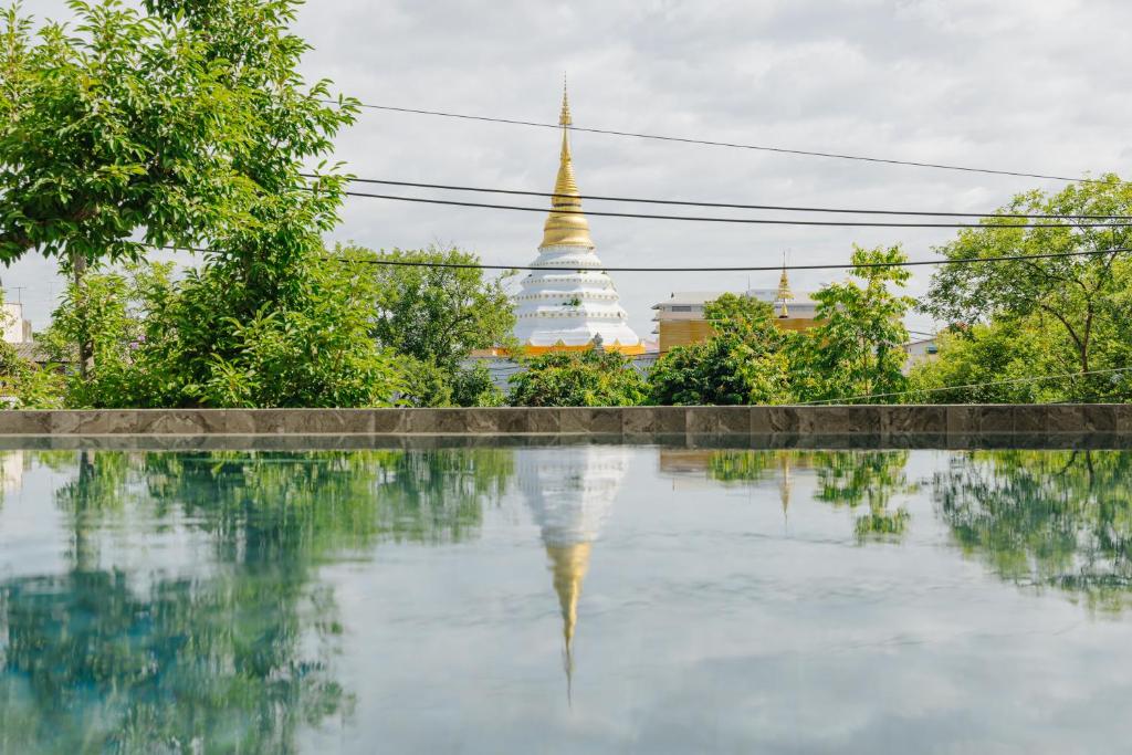A reflective pool looks toward a tree-lined view of a gilded temple spire.