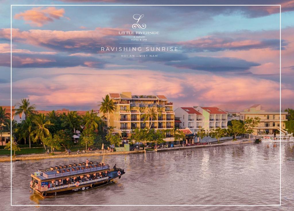 a boat on a river in front of a resort at Little Riverside Hoi An . A Luxury Hotel & Spa in Hoi An