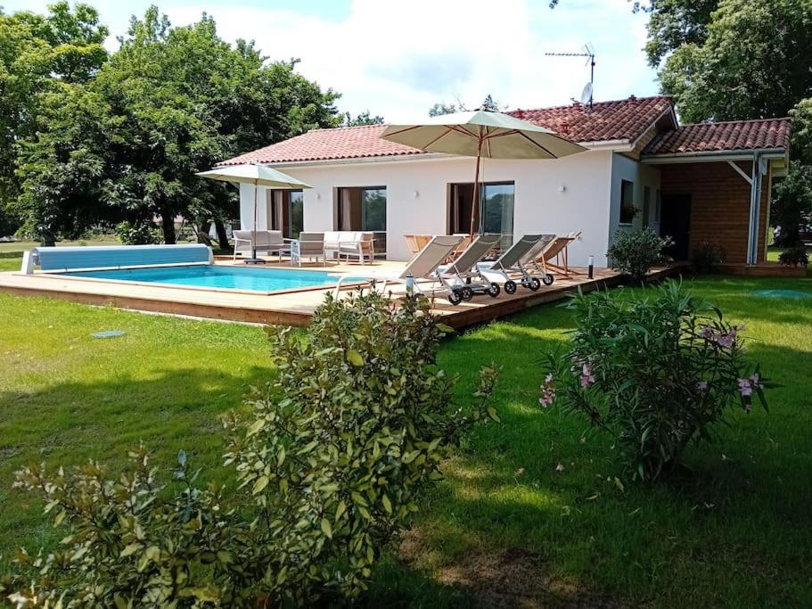 a house with a pool and chairs and an umbrella at Maison neuve avec piscine chauffée, 4 kms de Contis plage in Saint-Julien-en-Born