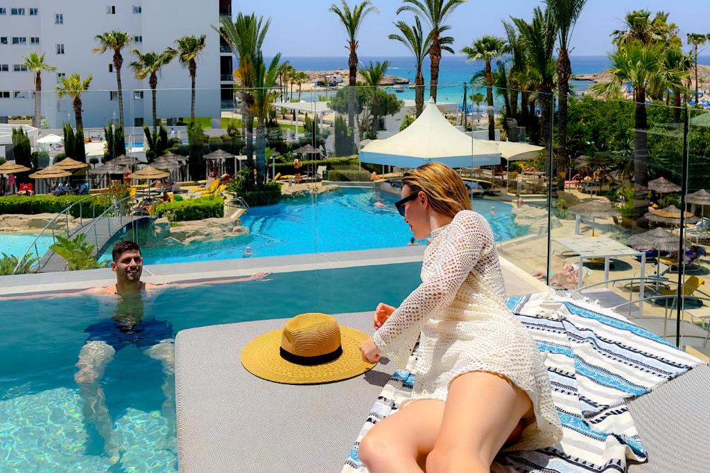 a woman in a hat sitting next to a swimming pool at Tasia Maris Beach Hotel - Adults Only in Ayia Napa