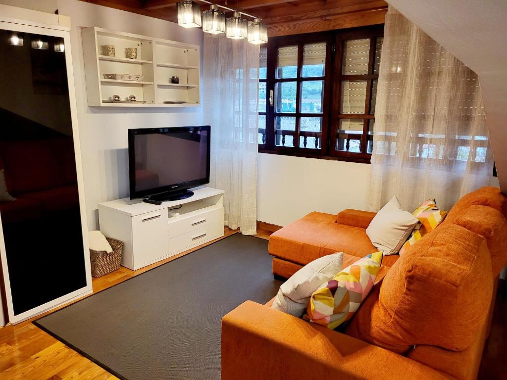 a living room with an orange couch and a flat screen tv at El mirador de la torre in Potes