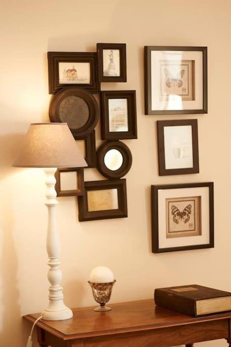 a table with a lamp and framed pictures on a wall at Gîte de la corgette in Saint-Romain