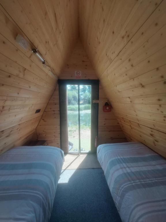 Habitación con 2 camas en una habitación de madera con ventana en Teeny Tiny Tipi lakeside pod, en Clare