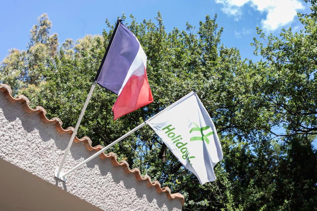 dwie flagi na dachu budynku z drzewami w tle w obiekcie Holiday Inn Perpignan, an IHG Hotel w Perpignanie