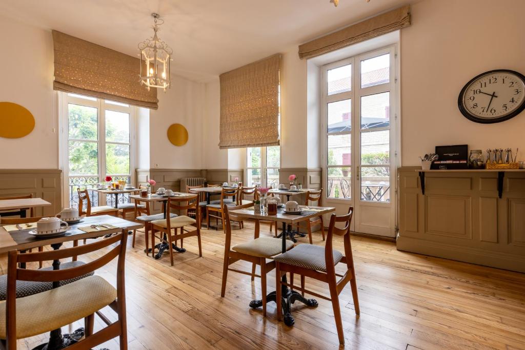 a restaurant with tables and chairs and a clock on the wall at Hôtel & Espace Bien-être La Maison du Lierre in Biarritz