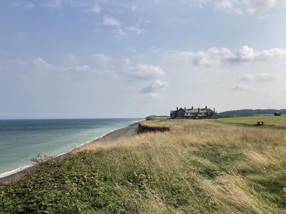 a house sitting on top of a bluff next to the ocean at Cliff-top Coastguard's Cottage, an Off-Grid Escape in Weybourne