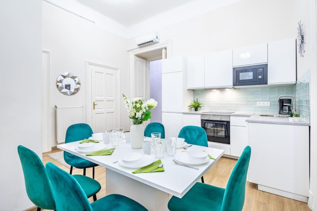 a white dining room with a white table and blue chairs at Cityscape Apartments Theresa in Budapest