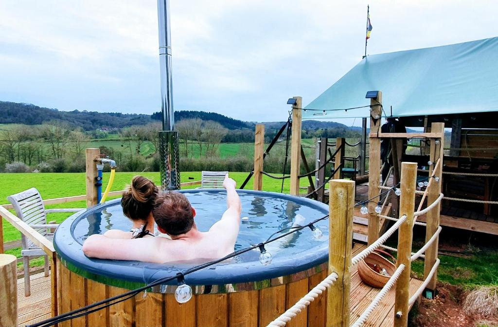 a man and a woman sitting in a hot tub at Hakuna Matata Safari Lodge - Sublime, off-grid digital detox with hot tub in Shelsley Walsh