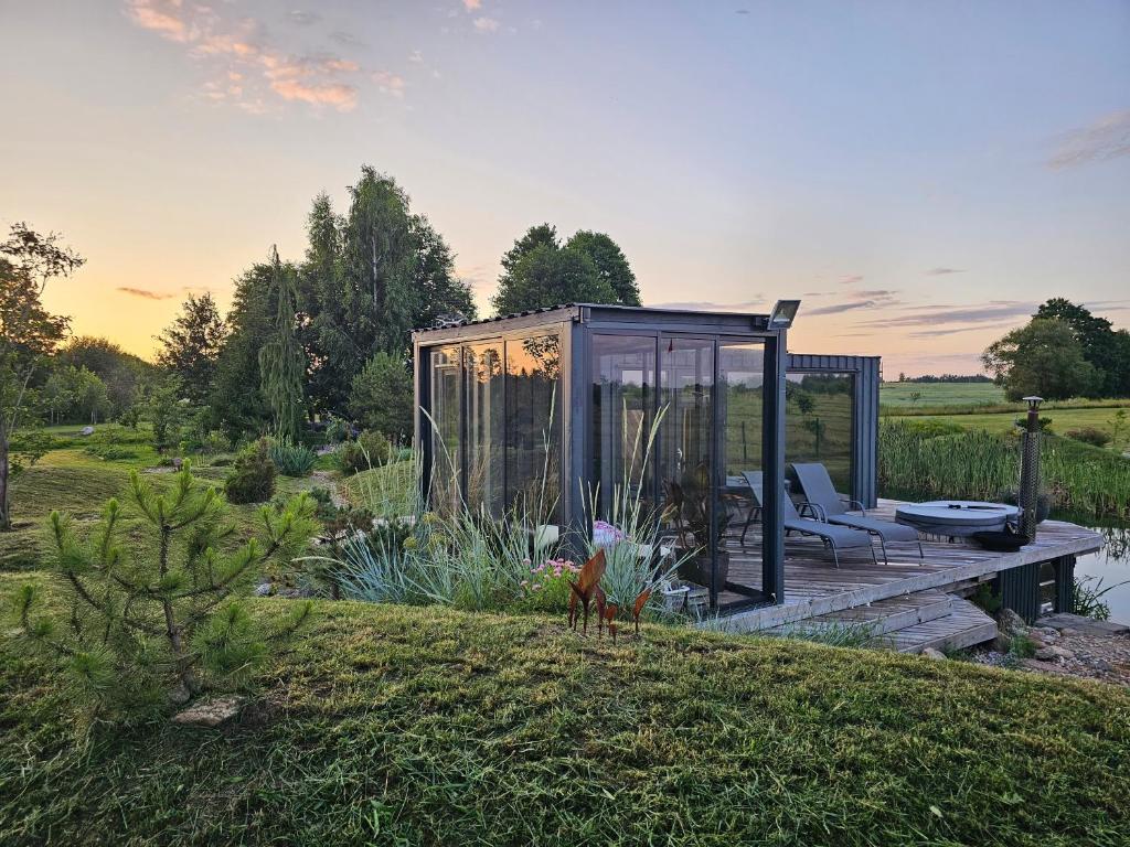 a glass house on a dock in a garden at Vaitų Riešutynė - Small shipping container house 