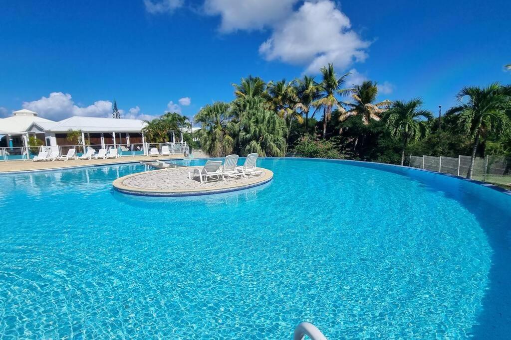 une grande piscine avec de l'eau bleue et des chaises blanches dans l'établissement La Mangotine - Duplex à Saint François avec piscine, à Saint-François