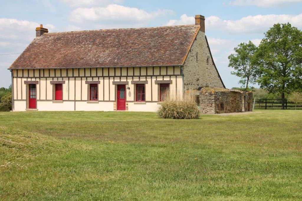 stary dom z czerwonymi drzwiami na polu w obiekcie Logement au coeur d'un haras avec accès à l'étang 