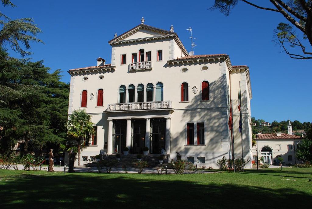 ein großes weißes Gebäude mit roten Fenstern auf einem Rasen in der Unterkunft Hotel Villa Soligo - Small Luxury Hotels of the World in Farra di Soligo