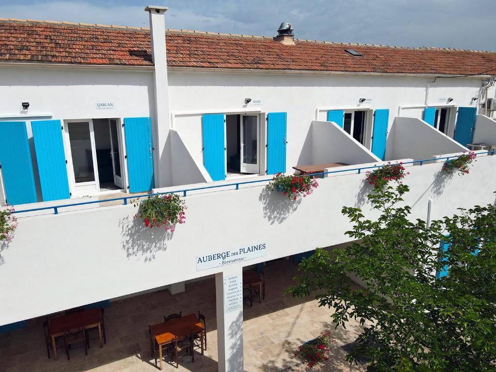 a white building with blue shutters and tables and chairs at Auberge des Plaines - Appartements avec terrasse in Arles