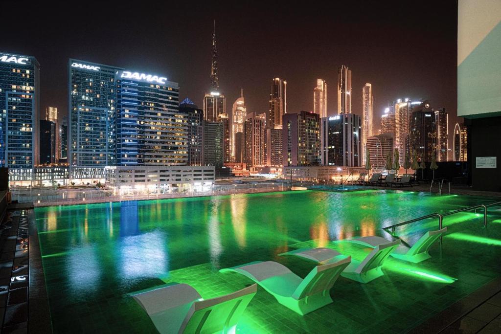 una piscina con sillas y un perfil urbano por la noche en The Suite Dubai 15 Northside Luxury Living en Dubái