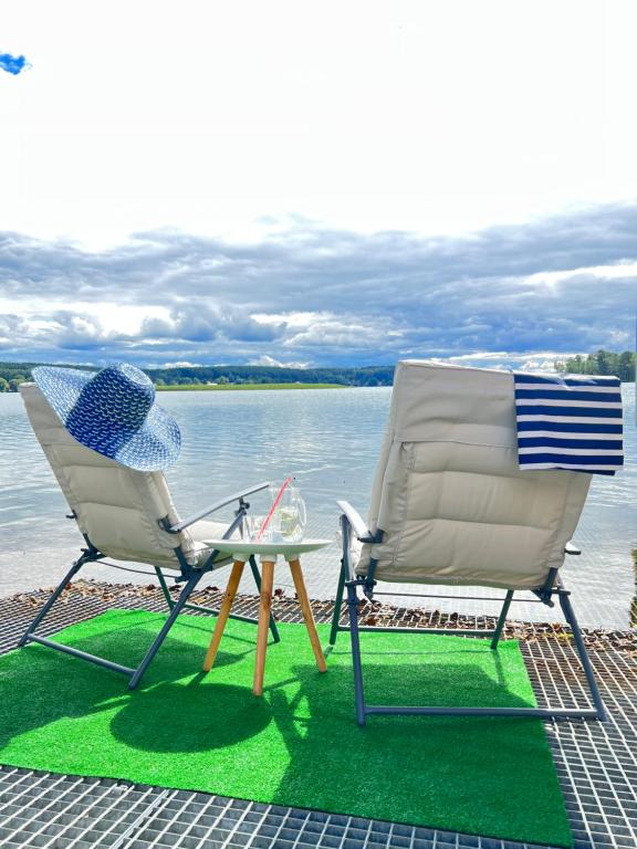 2 chaises et une table à côté de l'eau dans l'établissement Pokoje nad jeziorem z opcją szkolenia żeglarskiego, à Pluski