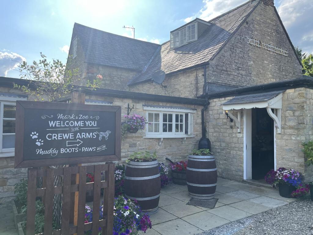 una casa de ladrillo con un cartel delante de ella en The Crewe Arms, en Hinton in the Hedges