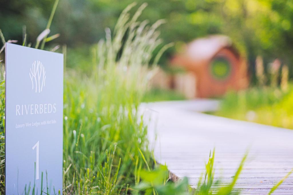 a sign in the grass with a house in the background at RiverBeds - Luxury Wee Lodges with Hot Tubs in Glencoe