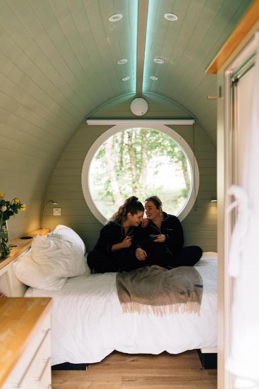 two women sitting on a bed in a room with a window at RiverBeds - Luxury Wee Lodges with Hot Tubs in Glencoe