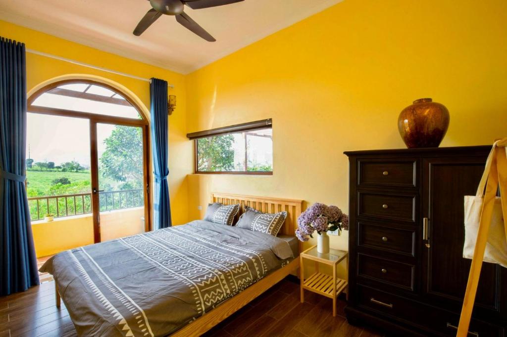 a bedroom with yellow walls and a bed and a window at Villa Mộc Châu Teahouse in Mộc Châu