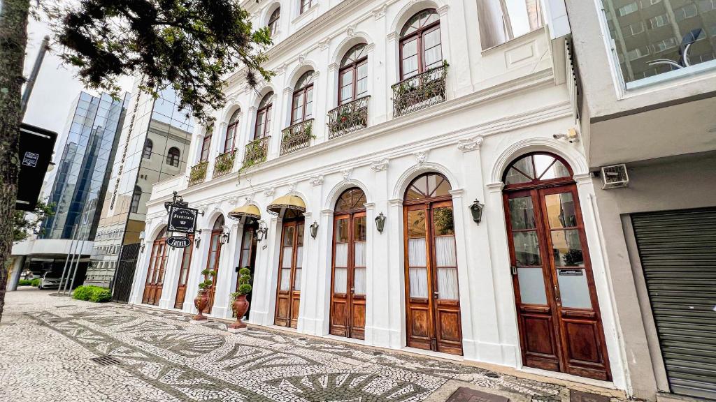 um edifício branco com portas de madeira numa rua em Johnscher by San Juan em Curitiba