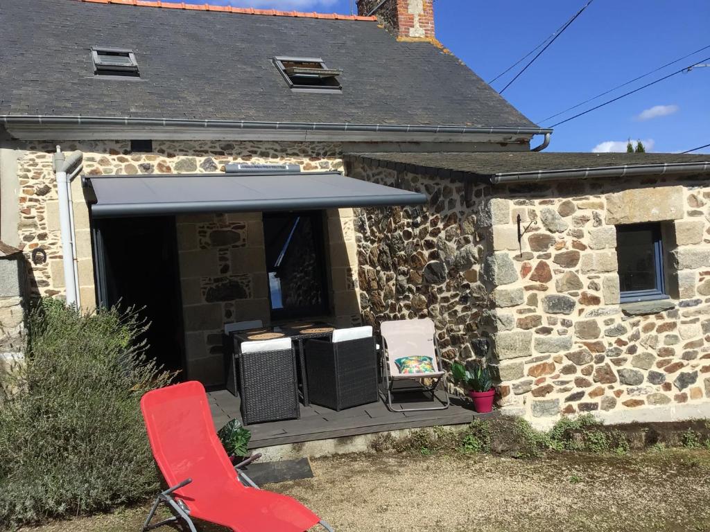 uma casa de pedra com um toldo e uma cadeira vermelha em Maison en pierre à la campagne proche de la mer em Plourhan