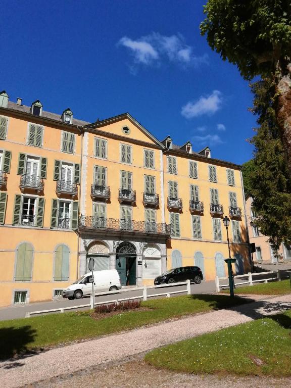 un grand bâtiment jaune avec des voitures garées devant lui dans l'établissement Appartement T2 eaux-bonnes, à Eaux-Bonnes