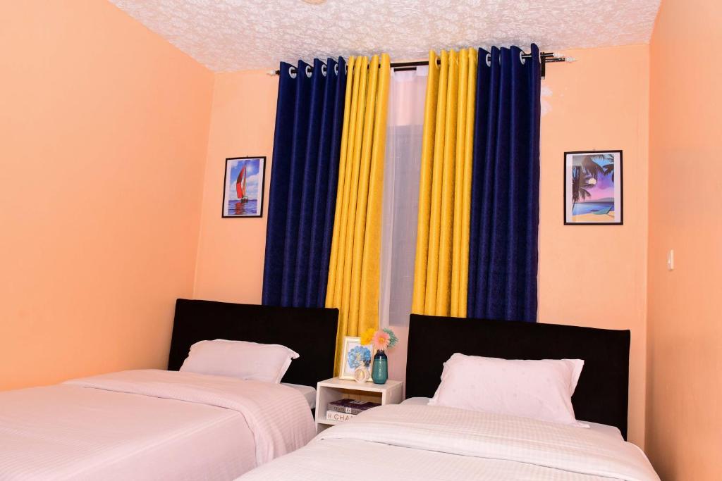 2 Betten in einem Zimmer mit blauen und gelben Vorhängen in der Unterkunft Modern & Homely Suite with Free Parking & WiFi in Embu