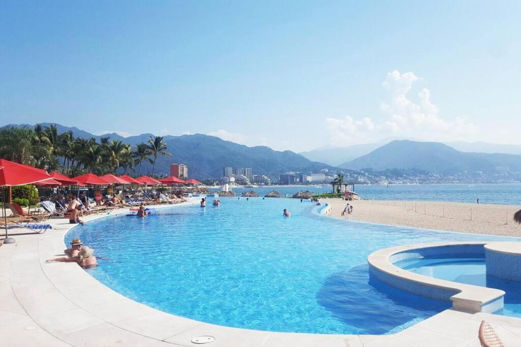 a swimming pool next to a beach with people in it at Grand Venetian - Zen oceanview condo in hotel zone in Puerto Vallarta