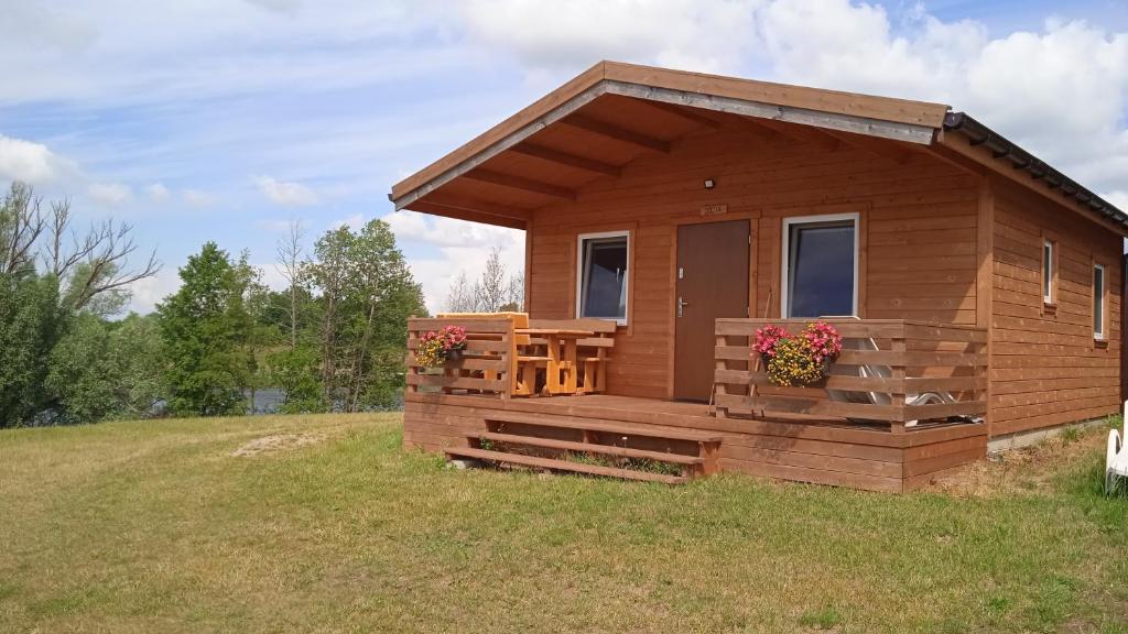 a wooden cabin with a deck on a field at Domek letniskowy Zełwągi in Zełwągi