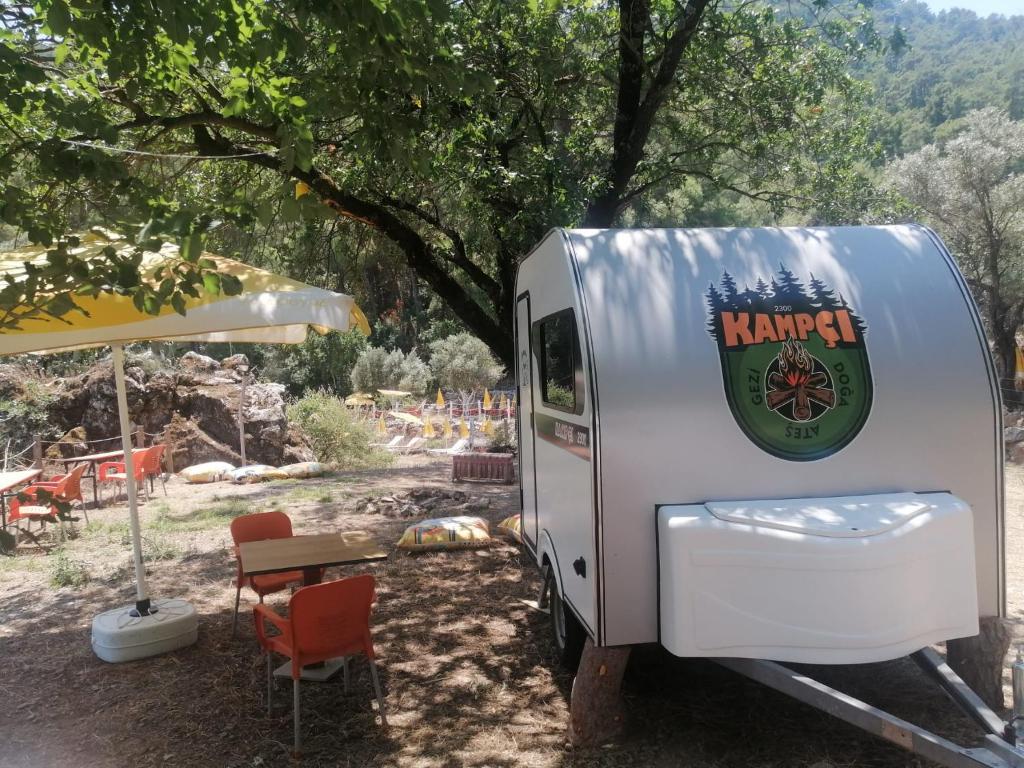 a white trailer parked under a tree with a table at Sultaniye Camping in Mugla
