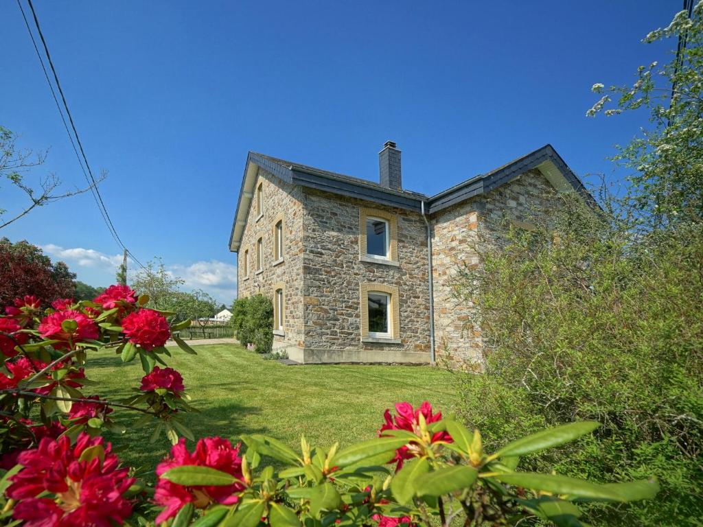 une ancienne maison en pierre avec des fleurs rouges devant elle dans l'établissement Bedecked Holiday Home in Vielsalm with Sauna, à Vielsalm