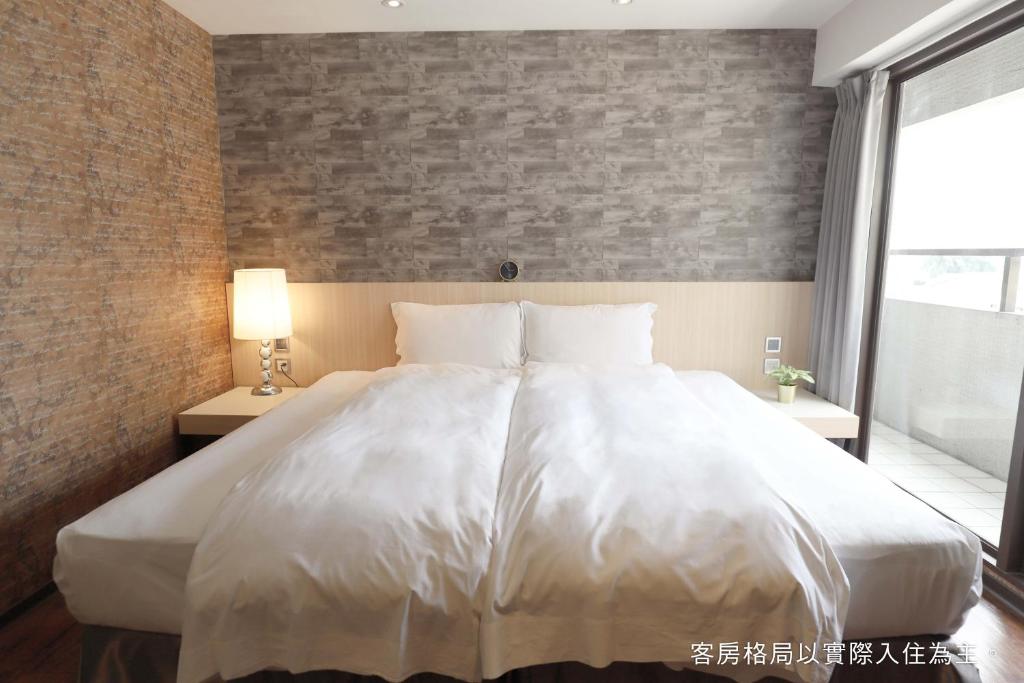 a large white bed in a bedroom with a brick wall at Talmud Hotel Yizhong in Taichung