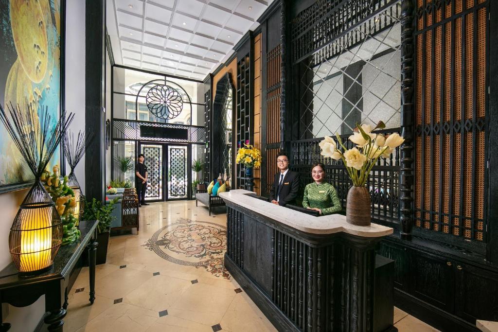 zwei Personen stehen in einer Lobby mit einer Theke in der Unterkunft Scent Premium Hotel in Hanoi