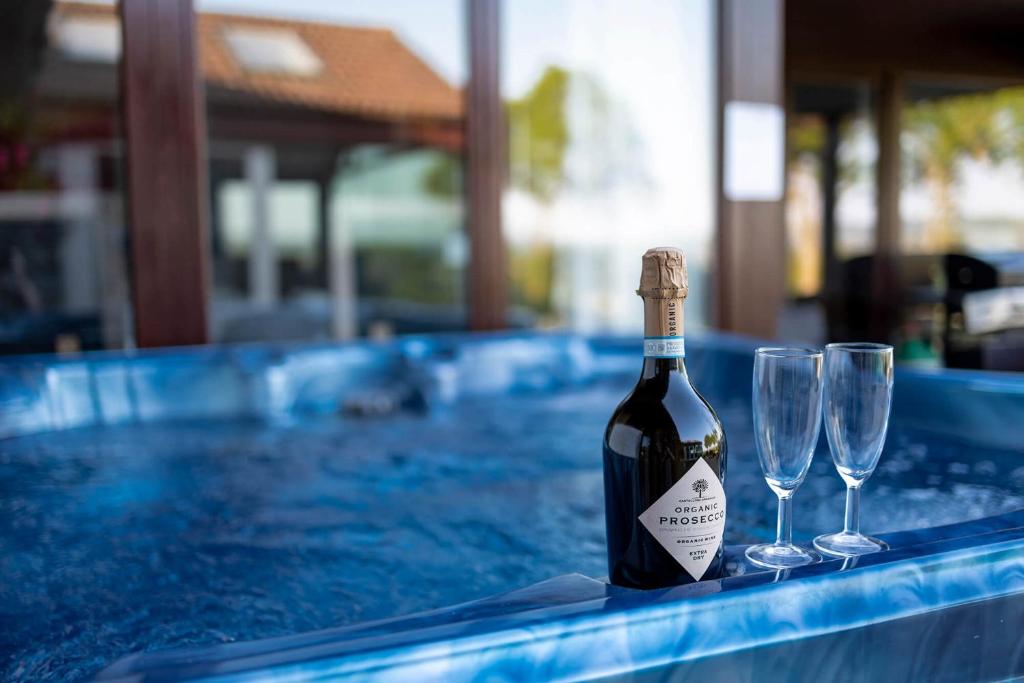 a bottle of wine and two wine glasses next to a swimming pool at Kingsley Lake View in Chew Stoke