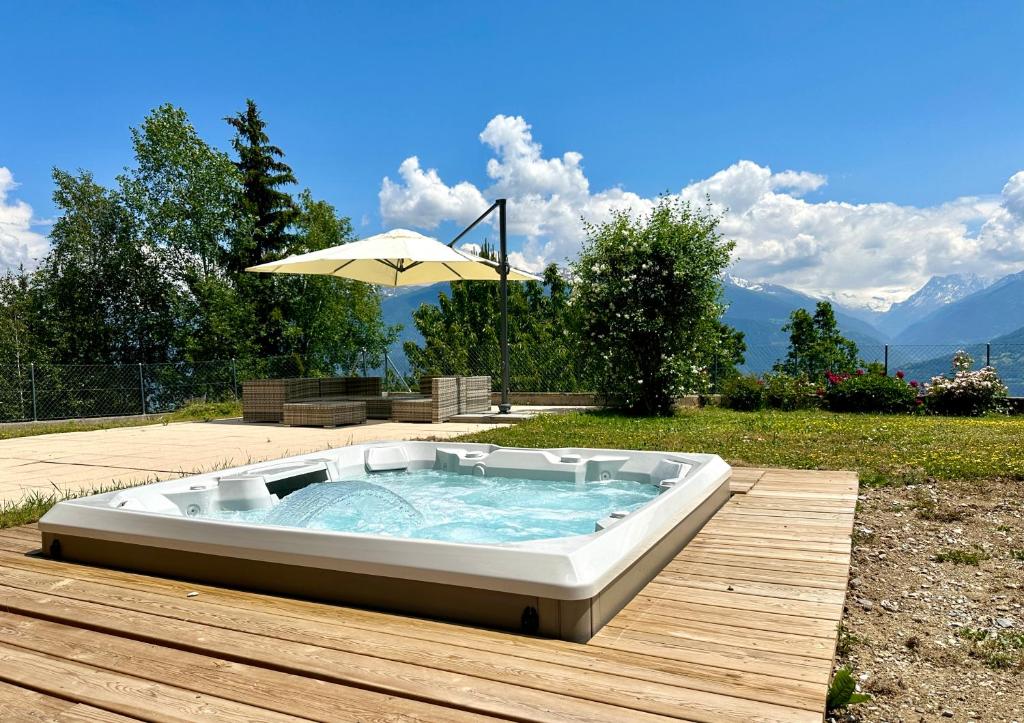 uma banheira de hidromassagem num deque de madeira com um guarda-sol em Le Chalet Pouchignon l Jaccuzzi l 6pers. em Savièse