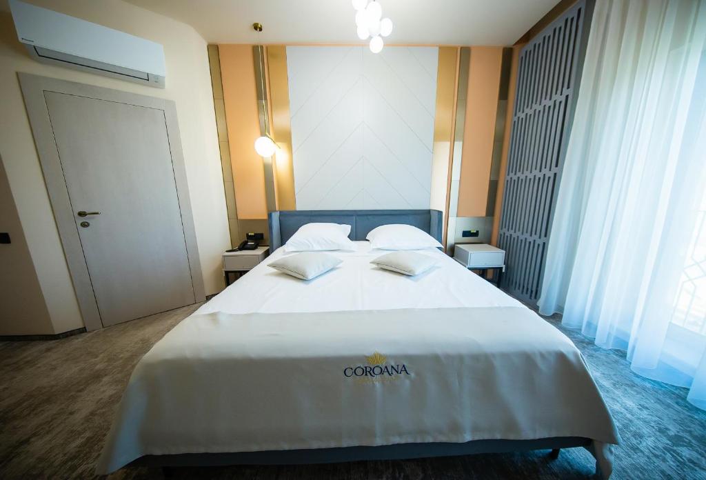 una habitación de hotel con una cama grande con sábanas blancas en Hotel Coroana, en Tîrgu Frumos