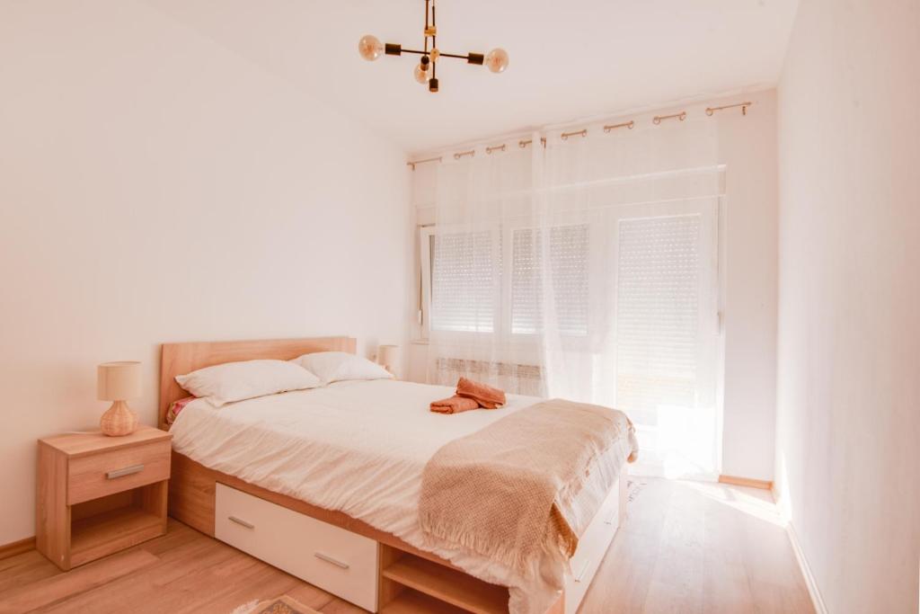 a white bedroom with a bed and a window at Apartman Platan in Metković