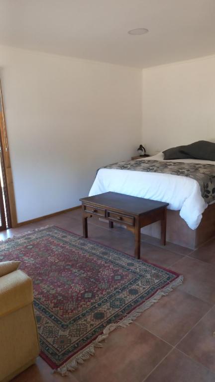 een slaapkamer met een bed met een tafel en een tapijt bij Refugio Gaia in Chillán