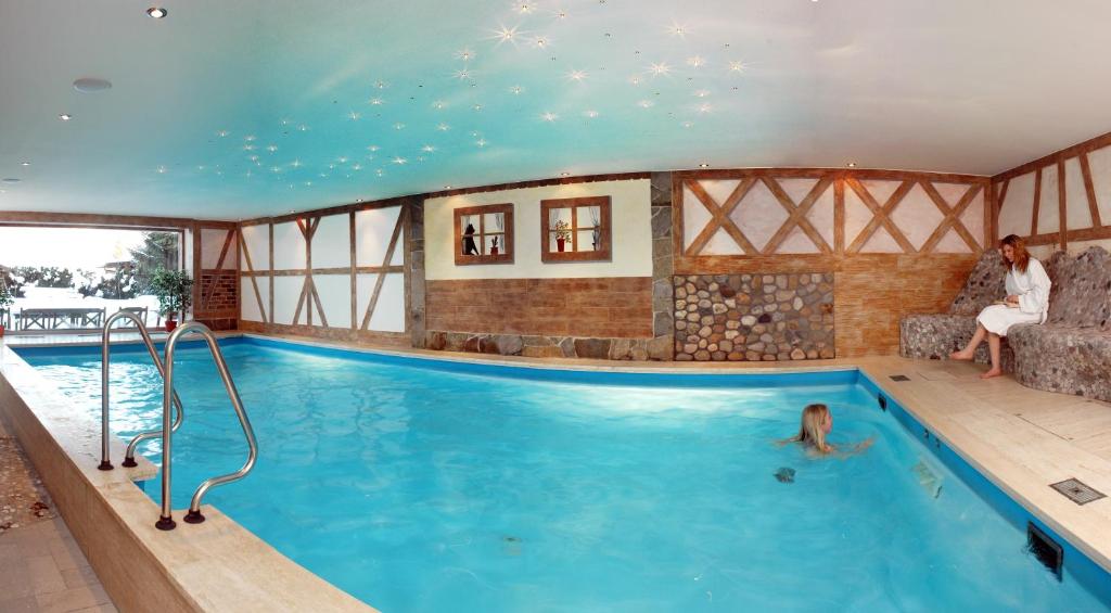a pool in a house with a woman sitting on a couch at Hotel AlpenSonne Ruhpolding in Ruhpolding