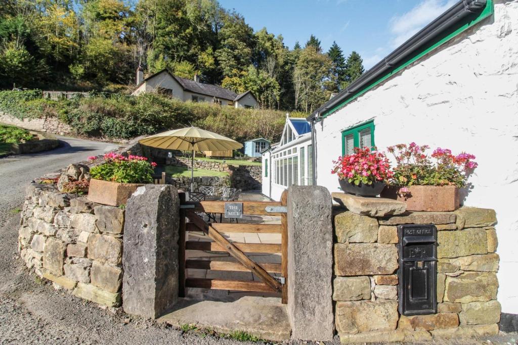 a stone wall with a wooden gate in front of a building at The Mill Nant Alyn in Rhydymwyn