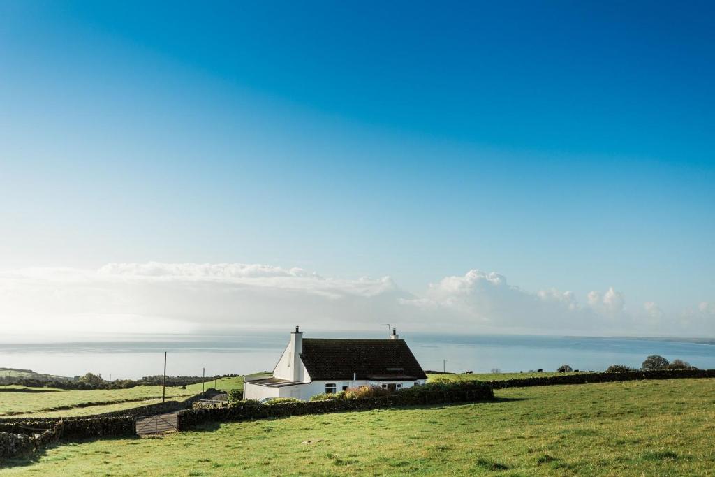 a house in a field with the ocean in the background at High Auchenlarie Cottage in Gatehouse of Fleet