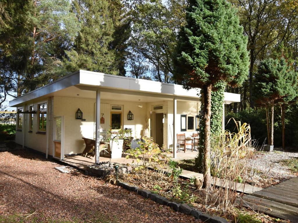 una pequeña casa blanca con un árbol delante en A detached bungalow with outdoor fireplace covered terrace and pond in a forest plot, en Wateren