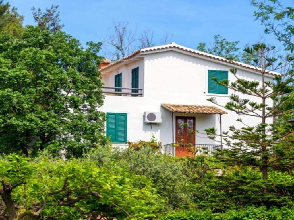 une maison blanche avec des volets verts et des arbres dans l'établissement Enticing Villa in Ricadi with Shared Swimming Pool, à Ricadi