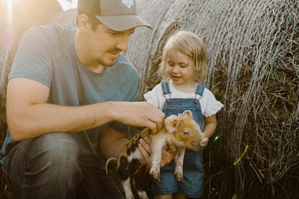 un homme et une petite fille tenant un bébé chèvre dans l'établissement Molitor Milk House- Feathered Acres Learning Farm & Inn, à Belgrade