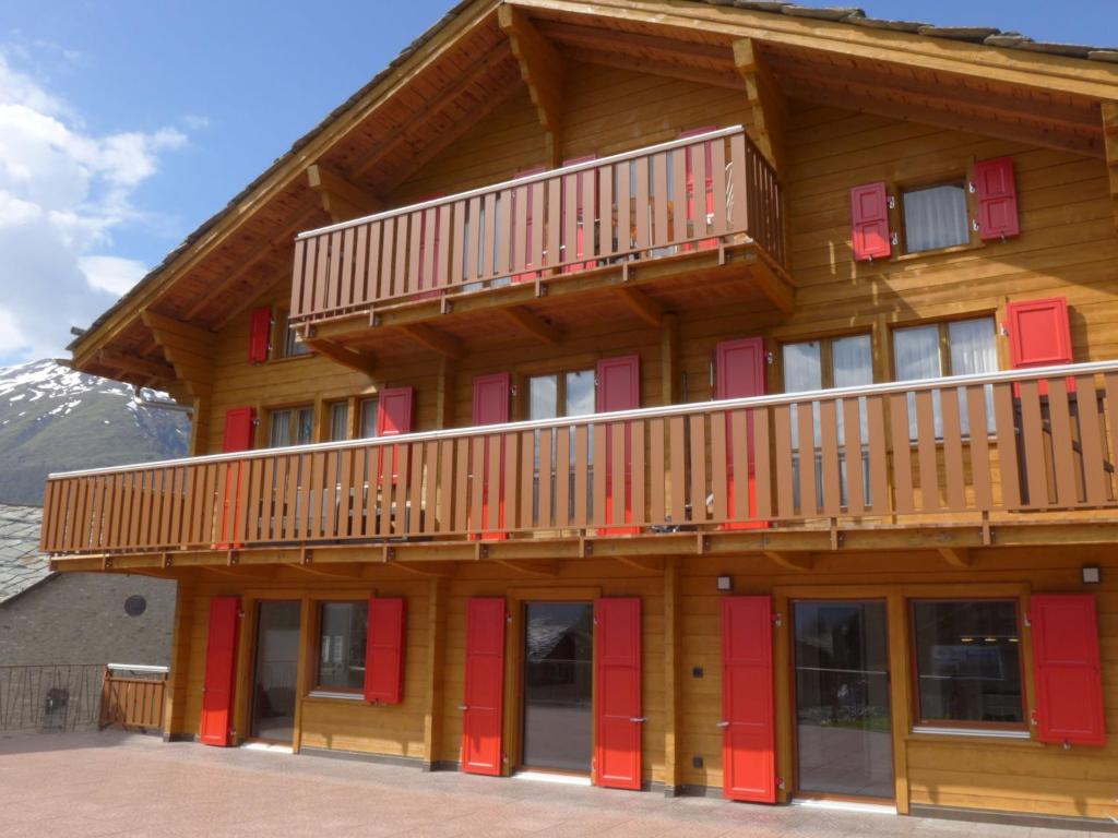 un gran edificio de madera con puertas rojas y balcón en Apartment Wiedersehn Dachgeschoss by Interhome, en Grächen