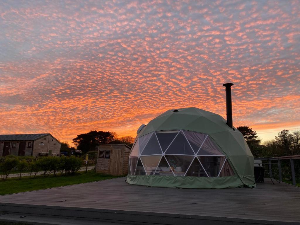 uma tenda num deque com um pôr-do-sol ao fundo em Glamping Dome Elysian Fields em Helston