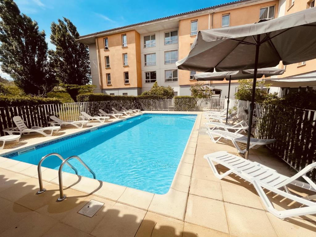 a swimming pool with lounge chairs and an umbrella at Zenitude Hôtel-Résidences Carcassonne in Carcassonne