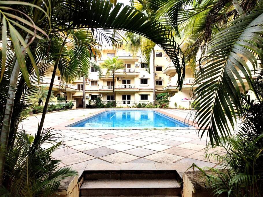 a swimming pool in front of a building with palm trees at #vrabode 1BHK apartment w Pool at Seacoast Retreat Varca in Talaulim